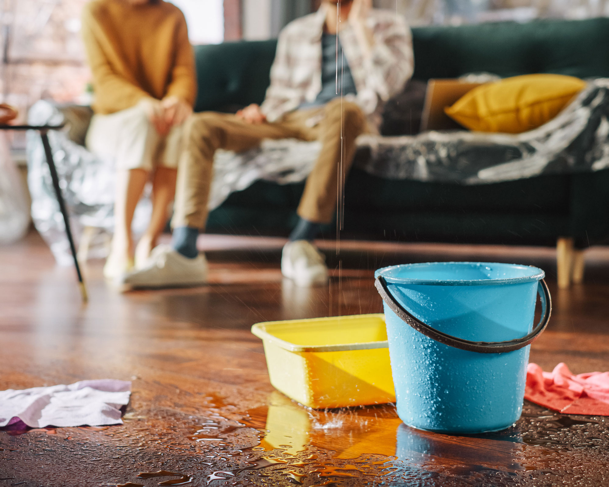 buckets catching leaks in a home with couple sitting on couch behind